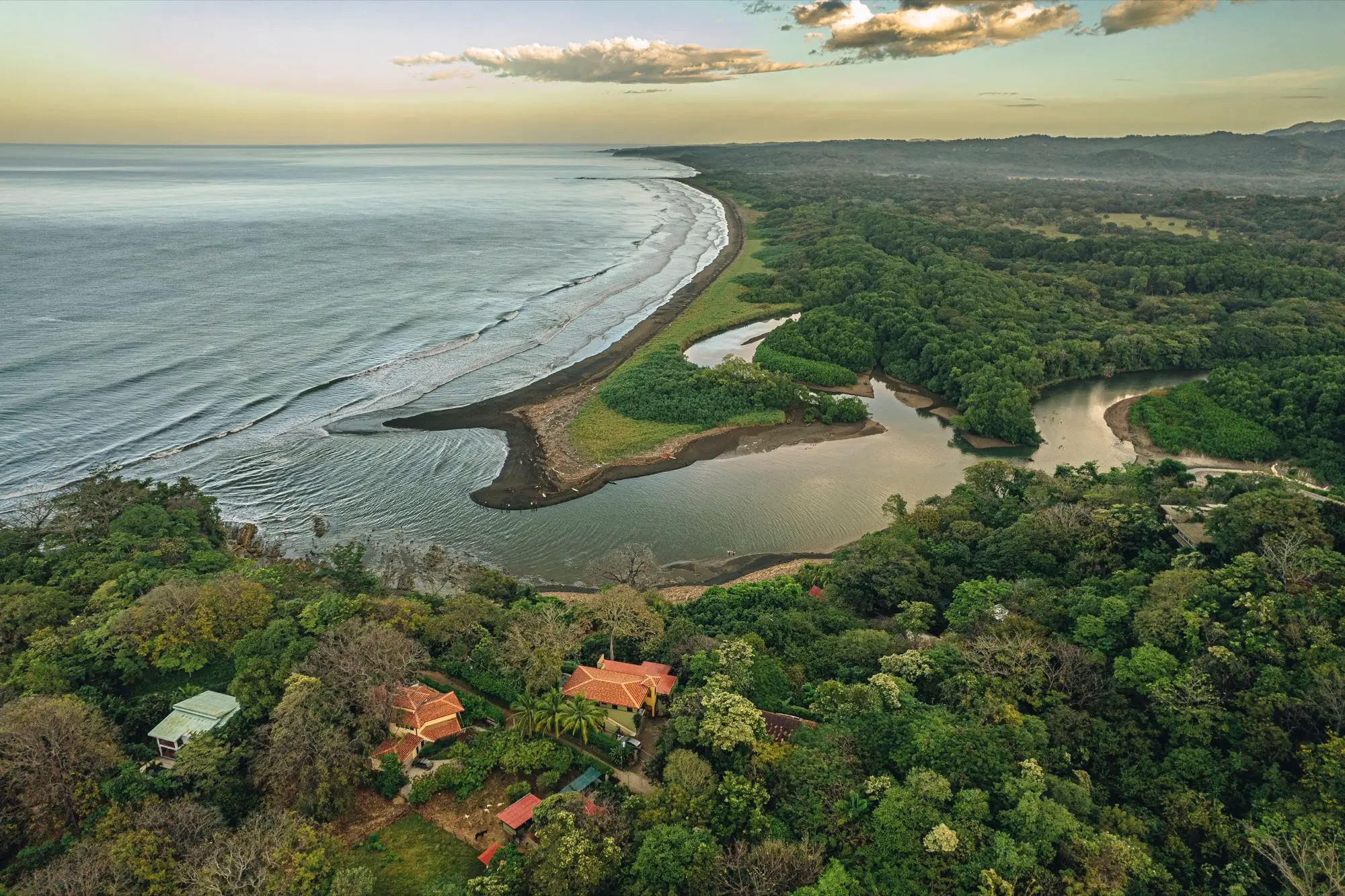 An aerial view of the Nosara coastline and river mouth, with Naya's rooftops visible in the jungle below